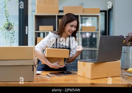 Happy Business asiatische Frau mit Paketversand-Box und spannend mit neuen Auftrag. Unternehmer Kleinunternehmen, die zu Hause arbeiten. Stockfoto