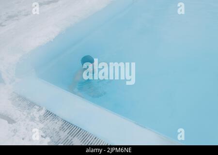 Fit Schwimmer männlichen Training schwimmen im offenen Winter Schwimmbad mit Nebel. Geothermisches Outdoor Spa Gesundheitskonzept. Stockfoto