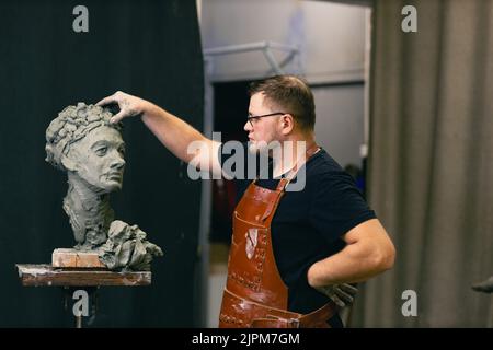 Mann Bildhauer schafft Skulptur Büste Ton menschliche Frau Skulptur. Werkstatt für die Erstellung von Statuen. Kleinunternehmen. Stockfoto