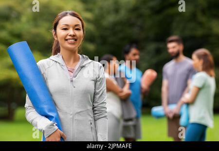 Lächelnde Frau mit Yogamatte über Gruppe von Menschen Stockfoto