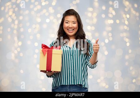Glückliche asiatische Frau mit Geschenkbox zeigt Daumen nach oben Stockfoto
