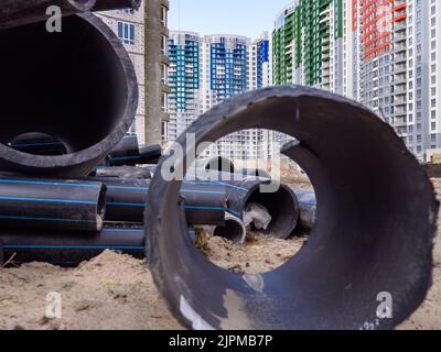 Blick durch ein riesiges schwarzes Rohr über die Baustelle mit neuen Hochhäusern im Hintergrund in Kiew, Ukraine. Neuer Bezirk im Bau Stockfoto