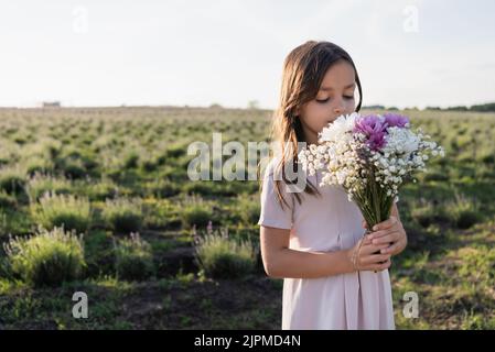 Brunette Mädchen in weißem Kleid riecht aromatischen Bouquet in Wiese Stockfoto