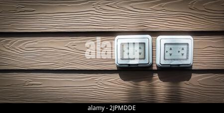 Wasserdichte Steckdosen, die im Freien an dunklen Holzwänden installiert sind. Stockfoto