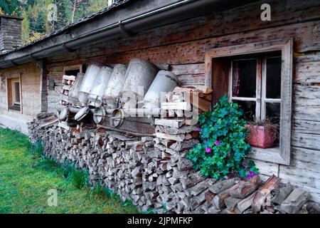 Ein traditionelles Holzhaus mit Brennholz und Milchkannen (Kirschen), vor der Gramai Alm (Gramaialm) in den malerischen Alpen in Österreich gestapelt Stockfoto