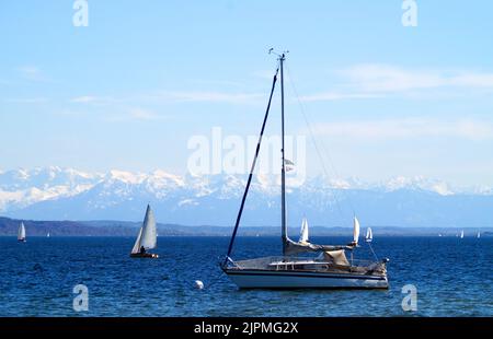 Wunderschöne Segelboote auf dem landschaftlich schönen und weiten Ammersee mit den verschneiten Alpen im Hintergrund an einem schönen Tag im April in Bayern, Deutschland Stockfoto