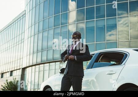 Porträt eines erfolgreichen afroamerikanischen Geschäftsmannes in einem Anzug in der Nähe seines Luxuswagens Stockfoto