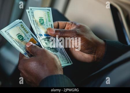Neuberechnung des verdienten Papiergeldes. Nahaufnahme der Hände eines Mannes, der Dollarscheine zählt. Das Konzept eines perfekten Geschäfts und der Rentabilität des Unternehmens. Stockfoto
