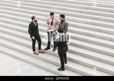 Geschäftstreffen im Freien. Eine Gruppe von Männern in Anzügen steht vor dem Hintergrund der städtischen Stufen einer großen Treppe. Arbeitspause. Teamarbeit Stockfoto