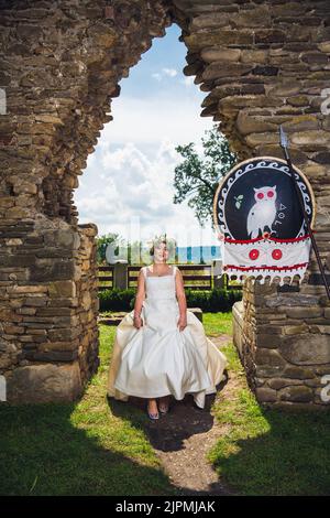 Eine kaukasische Braut, die ein weißes Hochzeitskleid trägt, während sie in einem Park sitzt Stockfoto