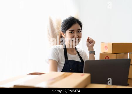 Portrait-Unternehmer lächelt und fühlt sich glücklich, während die Pakete für den Versand an Kunden vorbereiten. Junge Frau mit vielen Online-Bestellungen Stockfoto