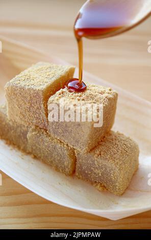 Köstliche japanische traditionelle Konfektion namens Warabimochi, die mit Kuromitsu-Sirup auf die Oberseite gegossen wird Stockfoto