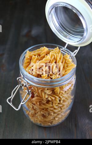 Ungekochte, getrocknete, ganze Weizenpaste aus Fusilli in einem Glaslagerkrül Stockfoto