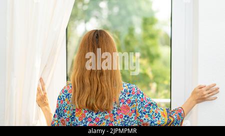 Eine junge Frau öffnet morgens die Fenstervorhänge Stockfoto