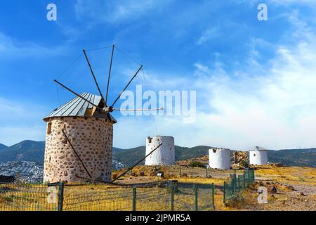 Reihe von traditionellen restaurierten Windmühlen der Stadt Bodrum in der Türkei. Alte Windmühlen auf einem Hügel am sonnigen Sommertag gegen blauen Himmel mit weißen Wolken. Reisen, Stockfoto