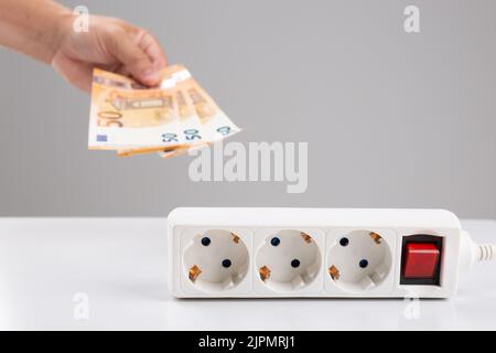Die Hand zeigt 50-Euro-Banknoten in der Nähe einer Steckdose. Steigende Strompreise und kostenintensives Energiekonzept Stockfoto