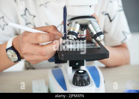 Nahaufnahme der unkenntlich Junge mit Cover slip während der Prüfung Substanz mit Hilfe moderner Mikroskop Stockfoto