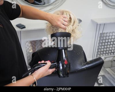 Eine Nahaufnahme eines Friseursalons, der die Haare einer blonden Frau im Salon trocknet Stockfoto