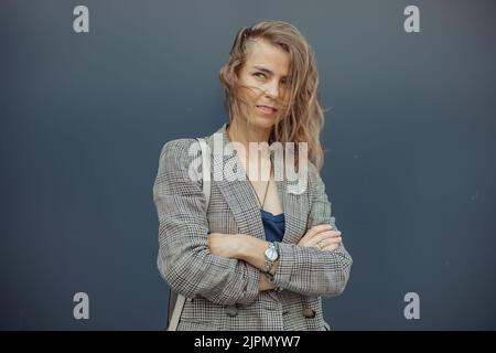 Porträt einer jungen, geheimnisvollen, schlanken Frau mit grünen Augen, die auf blauem Hintergrund mit gekreuzten Händen steht und posiert zur Seite schaut. Stockfoto