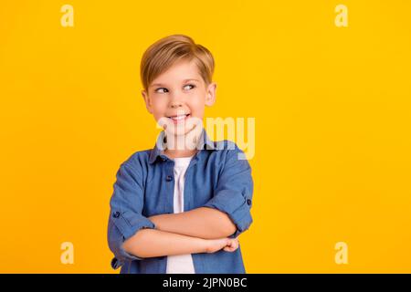 Foto von smart kreativ gesinnten Jungen gefaltet Arme toothy Lächeln suchen leeren Raum isoliert auf gelben Hintergrund Stockfoto