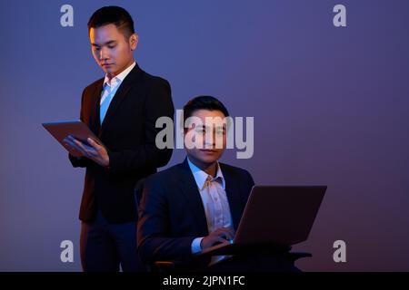 Hübsche junge Geschäftsleute mit Tablet und Laptop Stockfoto
