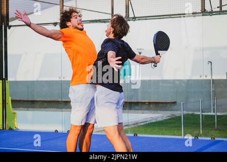 Portrait von zwei lächelnden Sportlern, die auf dem Padel Court im Freien mit Schlägern posieren - Padel-Spieler, die sich nach dem Sieg um ein Padel-Match freuen Stockfoto
