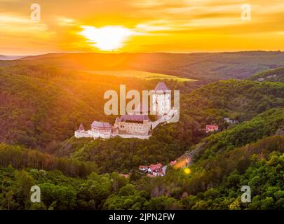 Luftaufnahme des wunderschönen Sonnenuntergangs über dem Schloss Karlstejn, Tschechische Republik. Drohne Aufnahme von alten Schloss mit in der Nähe von Wald. Burg im gotischen Stil war b Stockfoto