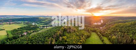 Luftpanorama von Karsltejn Burg mit in der Nähe Dorf und Wald, während der schönen Sonnenuntergang. Kleine Berge und See im Hintergrund. Wunderschön Stockfoto