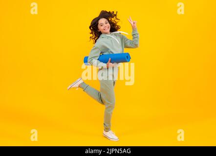 Mädchen Teenager im Trainingsanzug. Laufen und springen. Fröhliches, niedliches Kind in einem gelben Sportanzug auf gelbem Hintergrund. Sportbekleidung Werbekonzept. Stockfoto