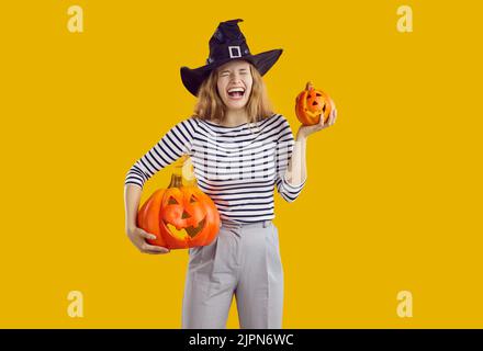 Porträt einer glücklichen, lustigen Frau in einem Hexenhut mit Halloween-Kürbissen und Lachen Stockfoto