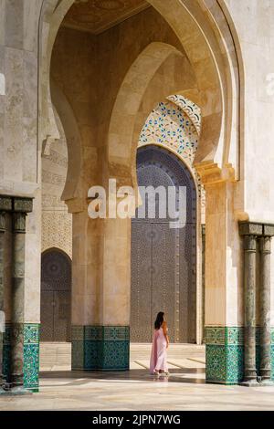 Ein Mädchen in einem schönen Kleid, das unter den hohen Bögen der Hassan II. Moschee in Casca steht Stockfoto