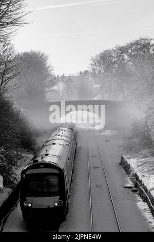 Im Morgennebel an einem verschneiten Tag fährt ein Zug mit drei Kutschen unter einer kleinen Brücke in Harrogate, North Yorkshire, England, Großbritannien. Stockfoto