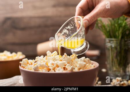 Geschmolzene Butter wird in einer Tonschüssel auf dem Küchentisch auf Popcorn gegossen Stockfoto