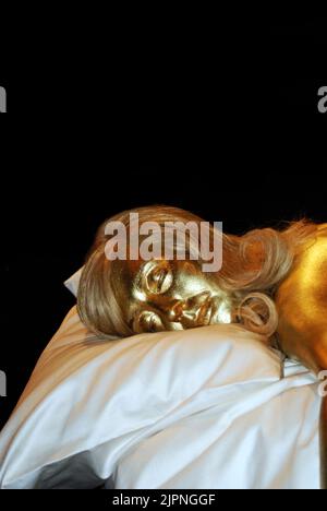 Aus Designing 007: 50 Years of James Bond Style, zeigt ein Modell der Schauspielerin Shirley Eaton, tot auf einem Bett liegend, aus der kultigen Szene in Goldfinger. Stockfoto