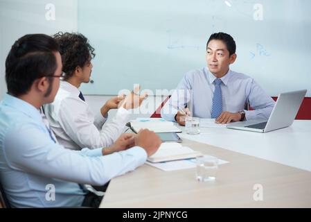 Reifer vietnamesischer Mitarbeiter, der den Ideen seiner Mitarbeiter zuhört Stockfoto