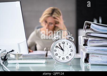 Wecker Vor Der Geschäftsfrau, Die Am Arbeitsplatz Arbeitet Stockfoto