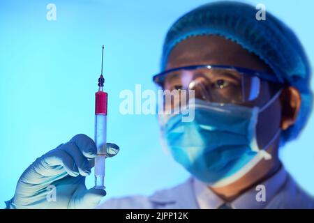 Nahaufnahme eines selbstbewussten medizinischen Mitarbeiters, der Schutzbrille trägt und die Spritze in der Hand hält, während er im Büro steht, Porträtaufnahme Stockfoto