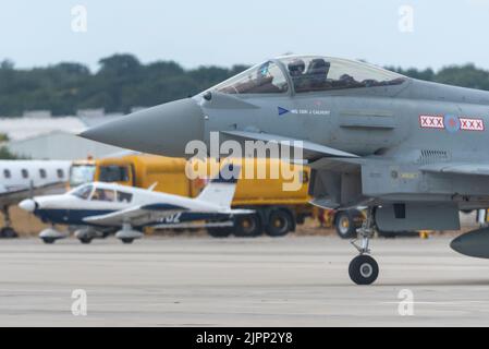 London Southend Airport, Essex, Großbritannien. 19. August 2022. Die Taifun-Düsenjäger der RAF nutzen den zivilen Flughafen für die Airshows dieses Wochenendes in Eastbourne und Folkestone. RAF Typhoon-Kämpfer mit einem zivilen Leichtflugzeug, das einrollt Stockfoto