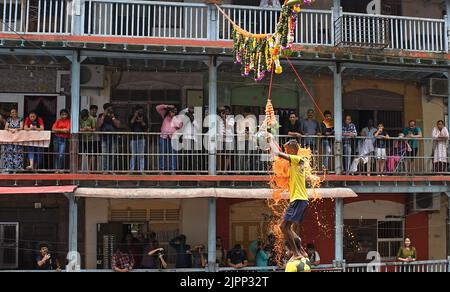 Mumbai, Indien. 19. August 2022. Ein Hindu-Anhänger, der auf einer menschlichen Pyramide steht, bricht Dahi handi (irdischer Topf mit Quark) während des Janmashtami-Festivals in Mumbai. Janmashtami wird gefeiert, um die Geburt von Lord Krishna zu markieren. Hinduistische Anhänger versammeln sich auf den Straßen und bilden akrobatische Pyramiden, um Dahi handi (irdischer Topf mit Quark gefüllt) zu brechen, um den Anlass zu feiern. Kredit: SOPA Images Limited/Alamy Live Nachrichten Stockfoto