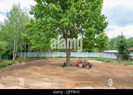 Minitractor auf einem bebauten Grundstück neben einem Baum. Stockfoto