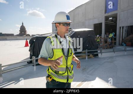 Austin Texas USA, August 2 2022: Bauleiter trägt Sicherheitsweste und Hut, während er auf dem Gelände eines fast fertiggestellten neunstöckigen Bürogebäudes in der Innenstadt ist, während sich der Bauboom in der texanischen Hauptstadt fortsetzt. In Austin befinden sich mindestens zwei Dutzend Gebäude im Bau, weitere befinden sich auf dem Reißbrett. ©Bob Daemmrich Stockfoto