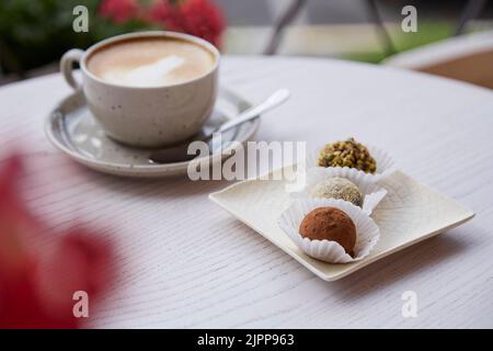 Natürliche vegane Trüffel ohne Backen, Mehl und Milch. Tasse Cappuccino auf einem Holztisch im Freien auf der Café-Terrasse. Kaffeepause Stockfoto