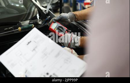 Mechanische Wartung mit einem Multimeter zur Überprüfung des Spannungspegels in der Autobatterie und der Auto-Dokumentation Stockfoto