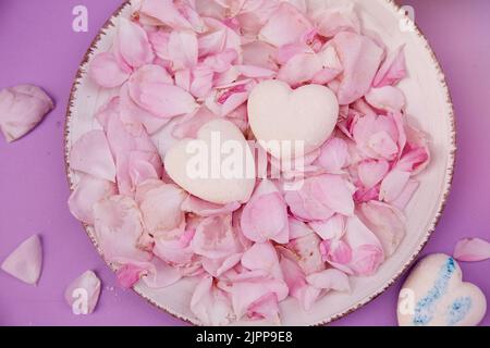 Hausgemachte natürliche zuckerfreie Vanille-Sümpfe Herzen auf Rosenblüten. Gesunde Süßigkeiten, natürliche Nahrung. Romantischer Hintergrund. Stockfoto