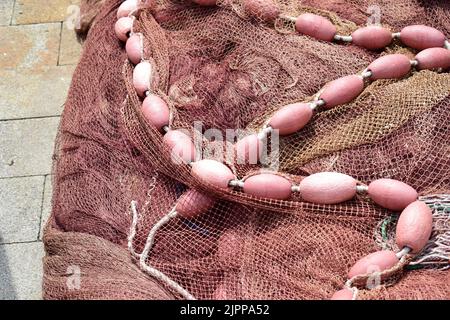 Nahaufnahme des alten rötlichen Fischernetzes mit kleinen Bojen. Stockfoto