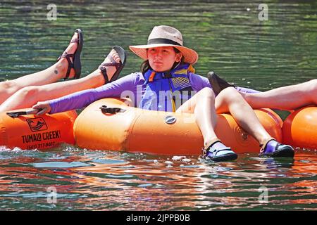 Junge Menschen treiben den Deschutes River in Bend, Oregon, auf leuchtend orangefarbenen Floatrohren und versuchen, der 100 Grad-F-Hitzewelle zu entkommen, die den pazifischen Nordwesten fegen wird. Stockfoto