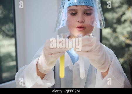 Intelligenter Schuljunge, der chemische Reaktionen in Reagenzgläsern beobachtet, hält er sich in den Händen seiner Handschuhen in der Chemiestunde Stockfoto