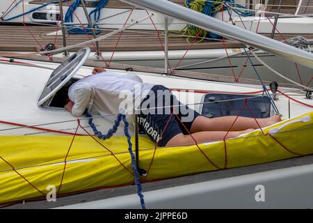 Crew-Mitglied bei der cowes Week Yachting Regatta, der durch eine Luke auf dem Deck einer großen Renn- oder Segelyacht blickt, Crew-Mitglied auf Yachtluken. Stockfoto