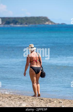 Ältere Frau im Bikini, die an der Küste der griechischen Insel Zante oder zakynthos an ihren jährlichen Sommerferien entlang läuft Stockfoto