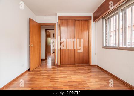 Leeres Schlafzimmer mit Einbauschrank mit Holzschiebetüren, französischem Eichenparkett, Aluminiumfenster mit Bars auf einer Seite und passendem Carpen Stockfoto